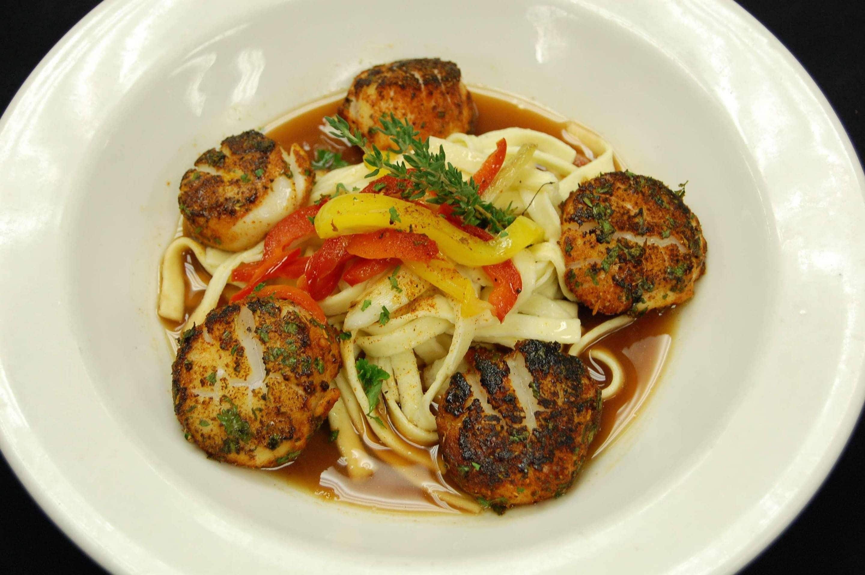 A plate of food with seared scallops, noodles, and sliced bell peppers.