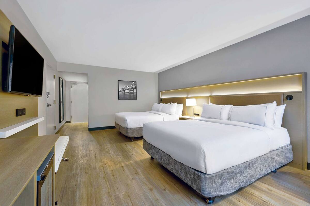 A hotel room with two beds, a flat-screen TV, a desk, and a framed picture on the wall.