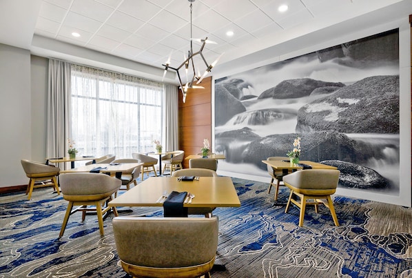 A hotel room with a large window, a dining area with tables and chairs, and a large wall mural of a waterfall.