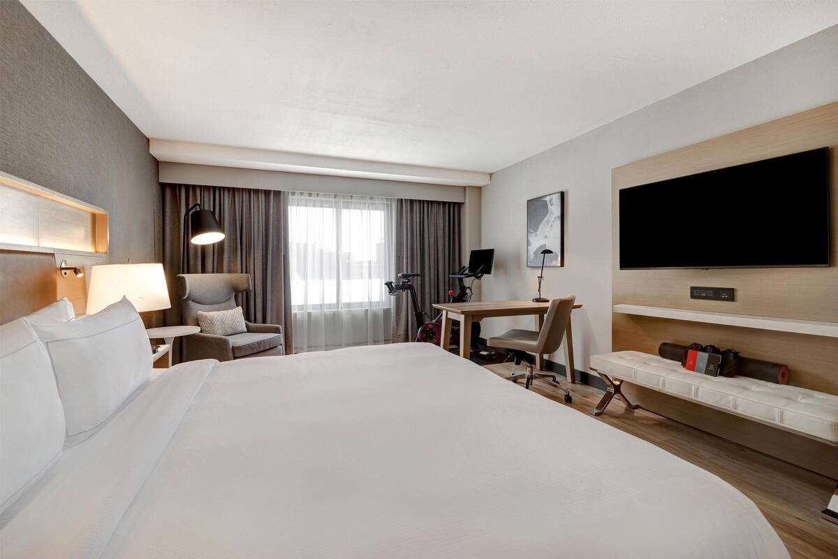 A hotel room with a large bed, a desk, a chair, a TV, and a window with curtains.