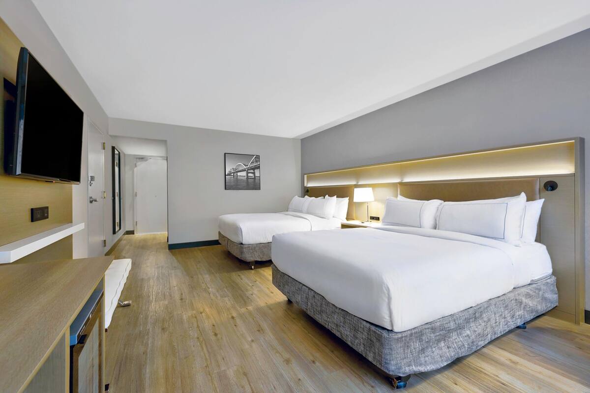 A hotel room with two beds, a TV, a desk, and a door leading to another room.