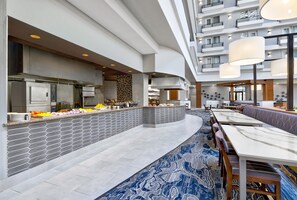 A modern hotel lobby with a central buffet, seating area, and a high-ceilinged atrium. - DoubleTree by Hilton Davenport (Davenport)