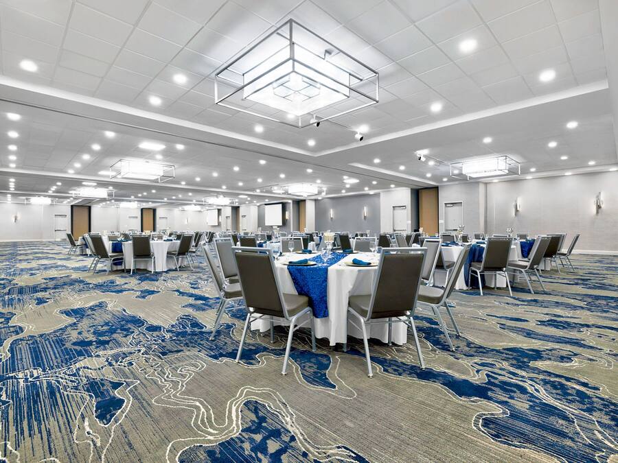 A large conference room with tables and chairs, a patterned carpet, and a high ceiling with recessed lighting.