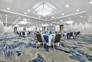 A large conference room with tables and chairs, a patterned carpet, and a high ceiling with recessed lighting.