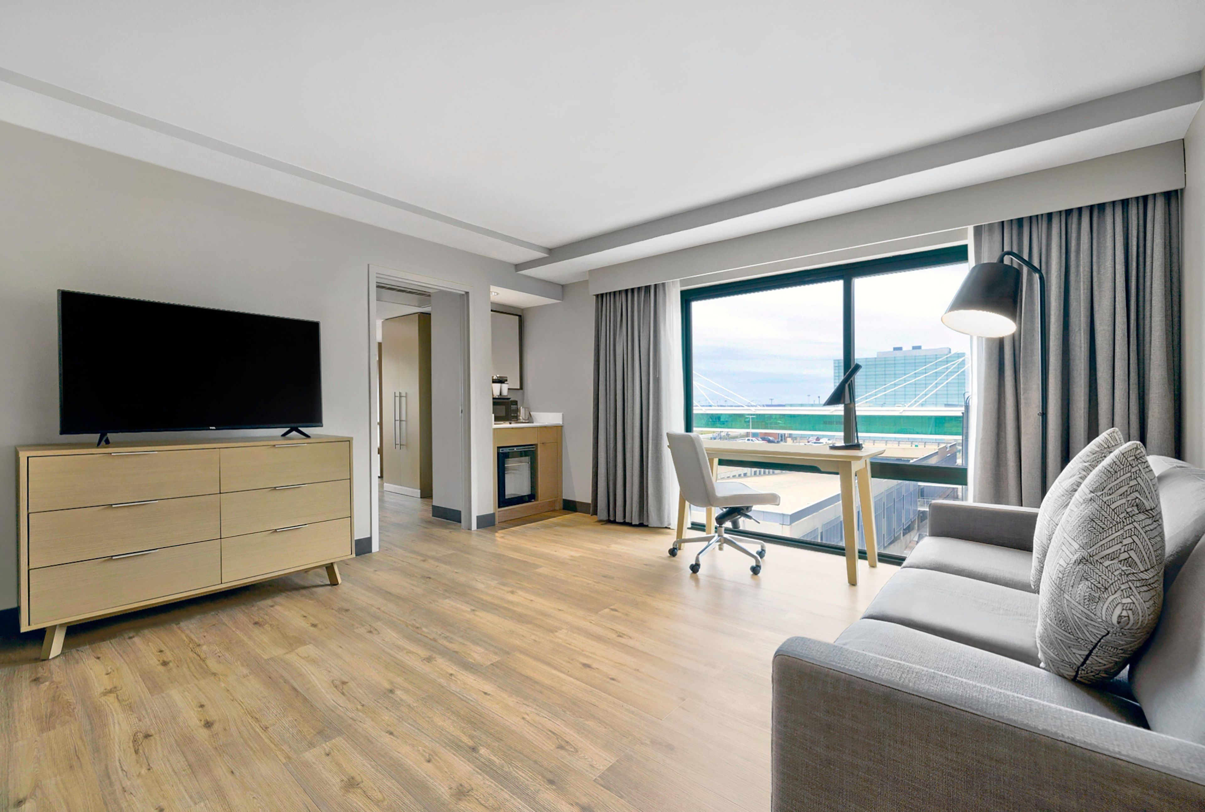 A modern hotel room with a flat-screen TV, a sofa, a desk, and a view of a bridge.