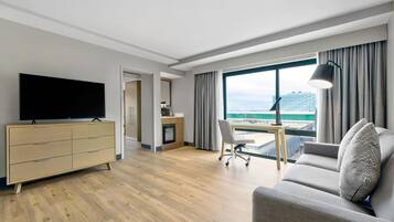 A modern hotel room with a flat-screen TV, a sofa, a desk, and a view of a bridge.