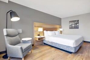 A hotel room with a bed, a chair, a nightstand, a lamp, and a framed picture on the wall. - DoubleTree by Hilton Davenport (Davenport)