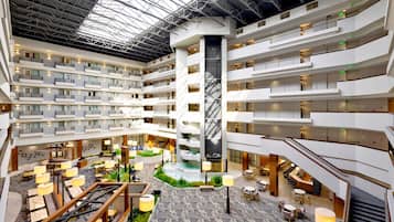 Ein mehrgeschossiges Hotel-Atrium mit einer zentralen Wasserspielen, mehreren Balkonen und unterschiedlichen Sitzgelegenheiten.
