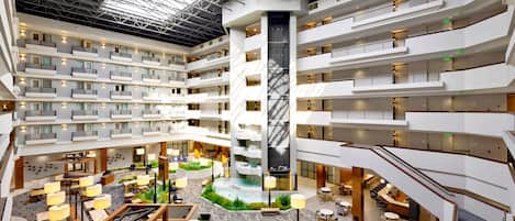 A multi-level hotel atrium with a central water feature, multiple balconies, and various seating areas.