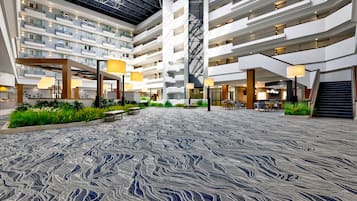 A multi-level hotel atrium with a central open space, multiple balconies, and indoor plants.