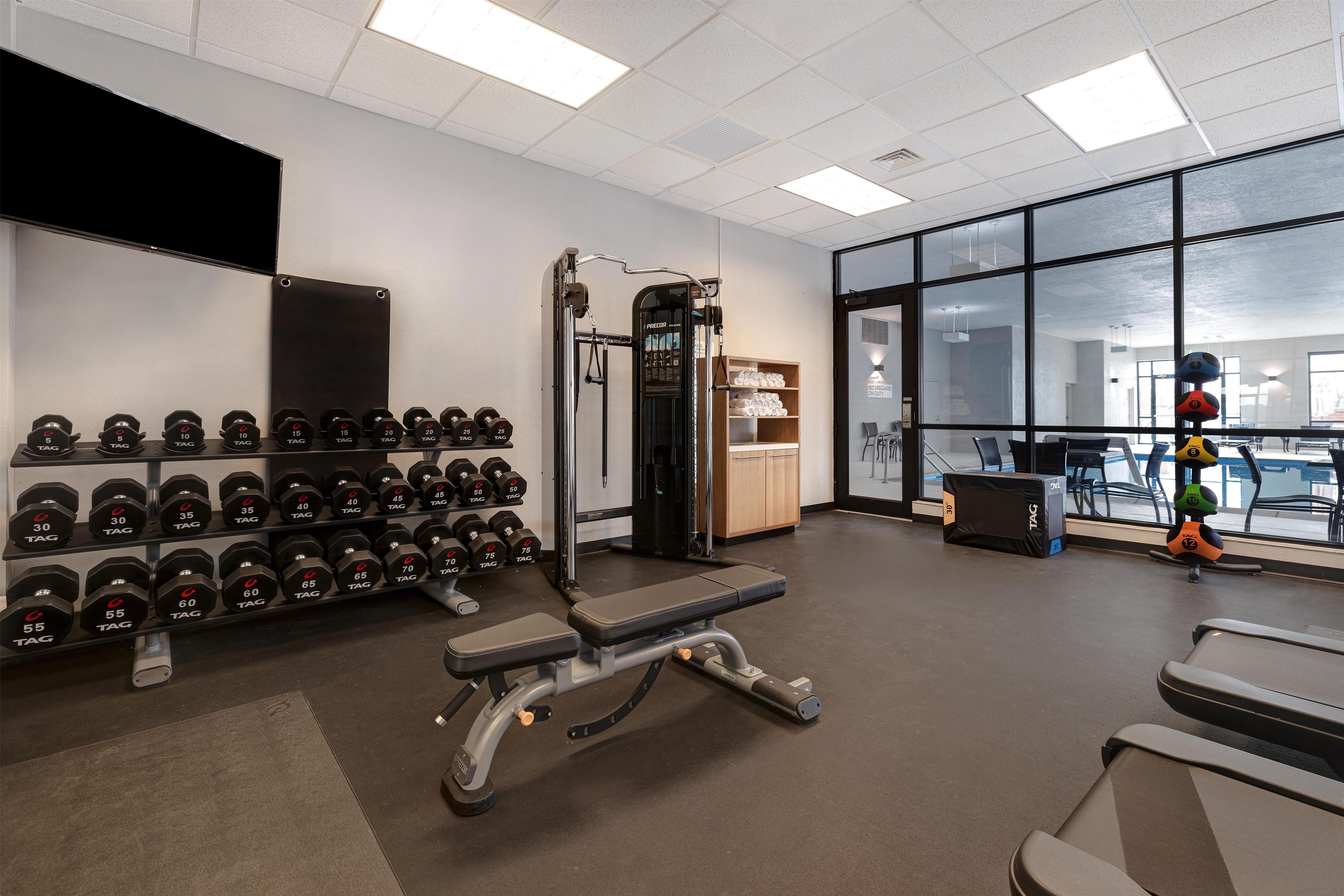 Uma academia com equipamentos de musculação, um banco e um suporte de halteres na parede.