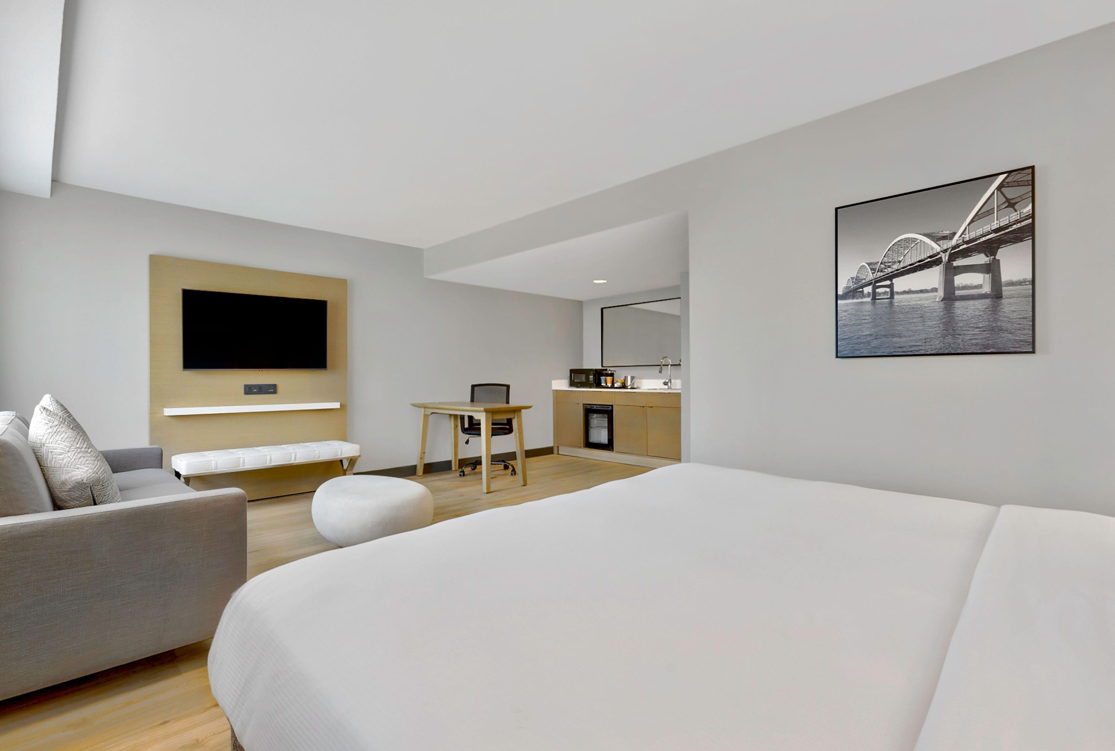 Una habitación de hotel moderna con una cama grande, un sofá, un escritorio y un televisor montado en la pared.