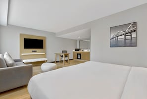 A modern hotel room with a large bed, a sofa, a desk, and a TV mounted on the wall.