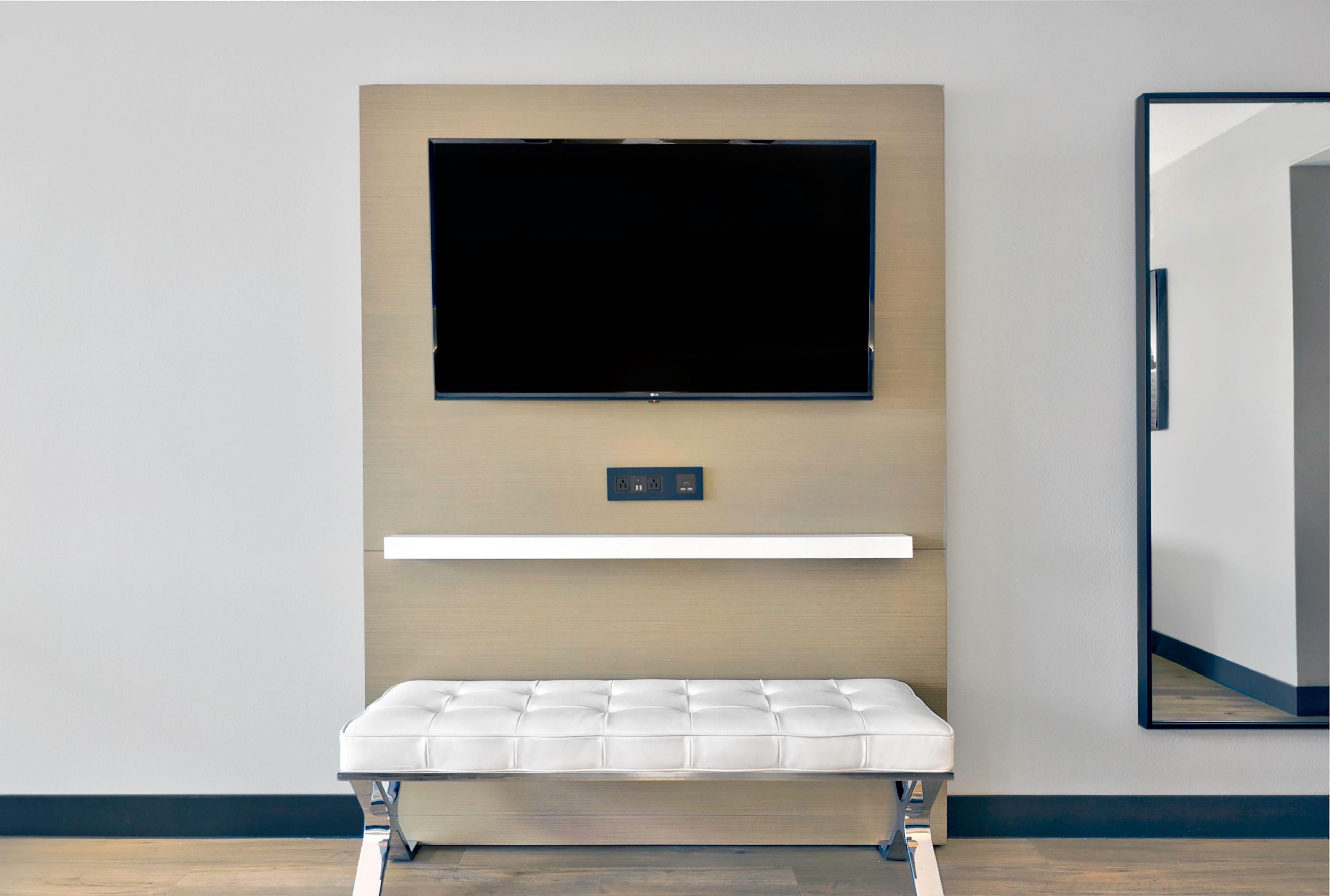 Una habitación moderna con un televisor montado, un banco y un espejo en la pared.