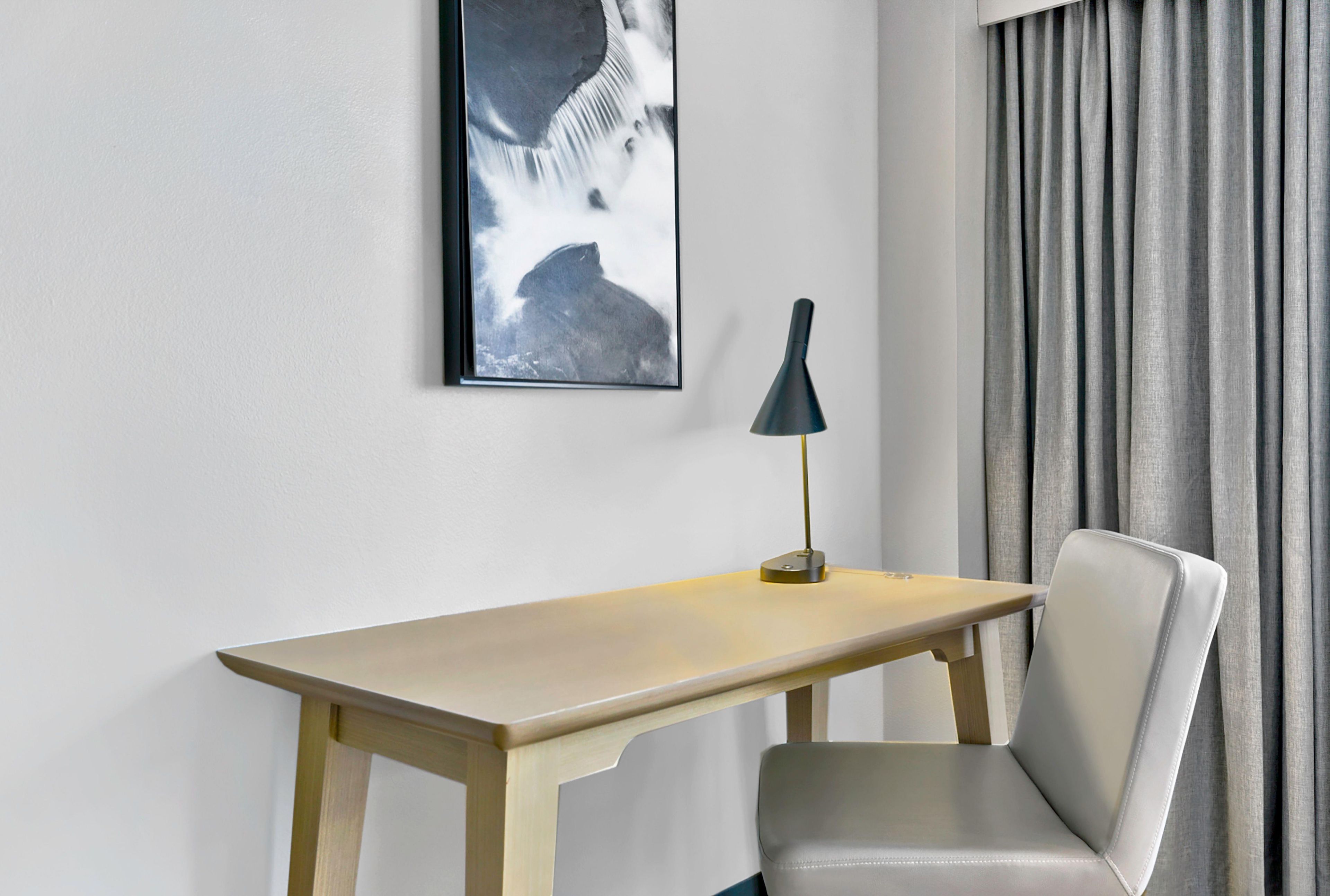 A room with a wooden desk, a chair, a framed picture, and a lamp.