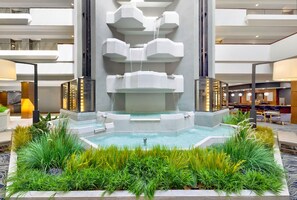 A modern indoor pool with a central waterfall, surrounded by lush greenery and a spacious, multi-level atrium. - DoubleTree by Hilton Davenport (Davenport)