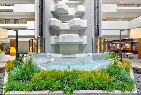 Piscina interior moderna con cascada central, rodeada de abundante vegetación y un amplio atrio de varios niveles.