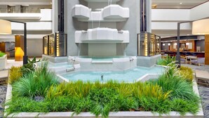 A modern indoor pool with a central waterfall, surrounded by lush greenery and a spacious, multi-level atrium. - DoubleTree by Hilton Davenport (Davenport)