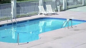 A rectangular pool with a tiled edge, surrounded by a white fence. There are two white lounge chairs and a metal pool ladder.