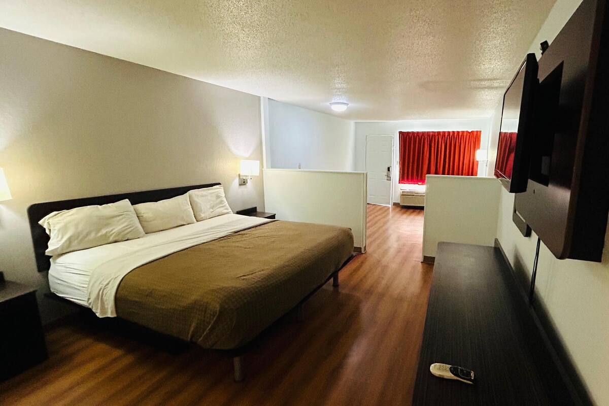 Habitación de hotel con cama, televisión, escritorio y ventana con cortinas rojas.