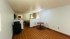 A compact living space with a kitchenette, a dining area with two chairs, and a bed in the background. - Super 7 Inn Tupelo (Tupelo)