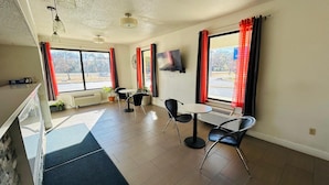 A hotel room with a large window, a flat-screen TV mounted on the wall, a small table with two chairs, and a potted plant. - Super 7 Inn Tupelo (Tupelo)