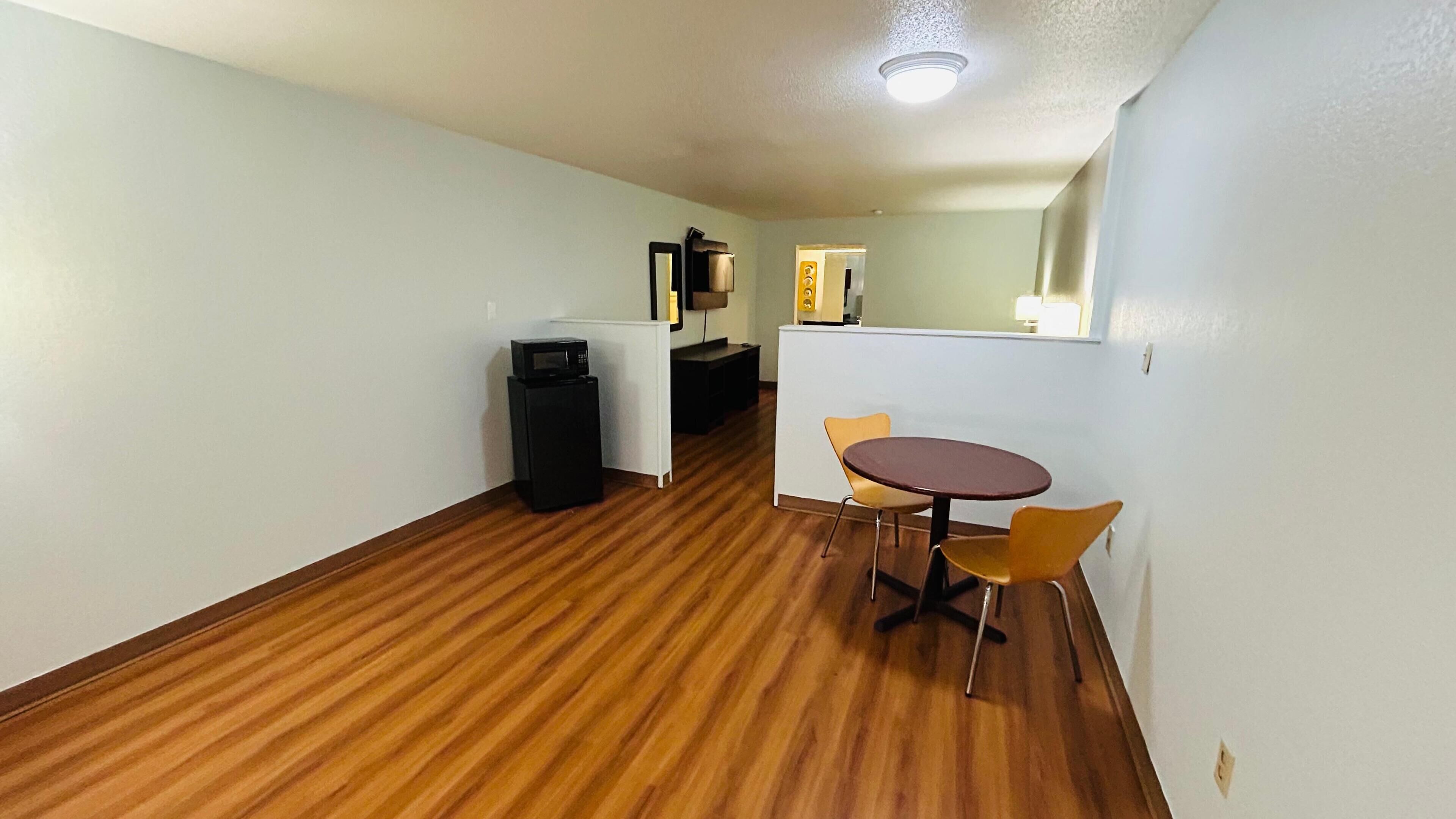 Habitación de hotel con piso de madera, una pequeña mesa redonda con dos sillas, microondas y un mueble auxiliar.