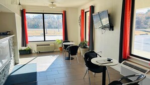 A room with a large window, a flat-screen TV, a table with chairs, and a potted plant. - Super 7 Inn Tupelo (Tupelo)
