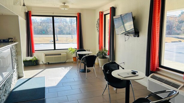 A room with a large window, a flat-screen TV, a table with chairs, and a potted plant. - Super 7 Inn Tupelo (Tupelo)