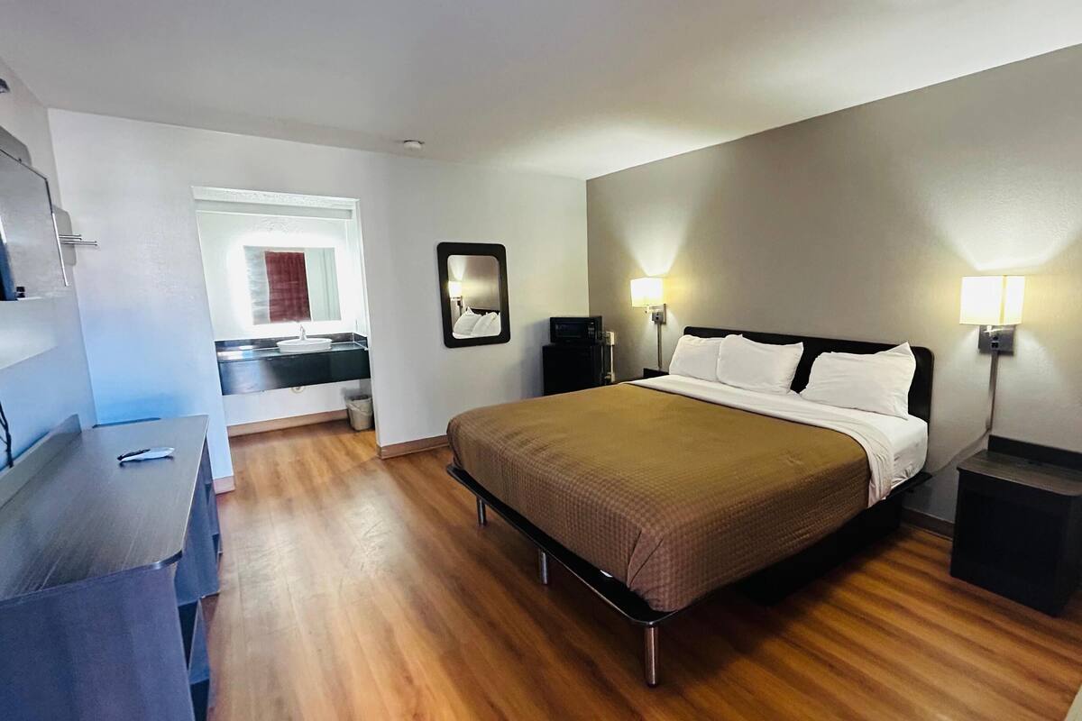 Una habitación de hotel con cama, lámparas de noche, escritorio y espejo.