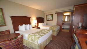 A hotel room with two beds, a desk, a chair, a television, and a bathroom visible through an open door. - Rosen Inn, closest to Universal (Orlando)