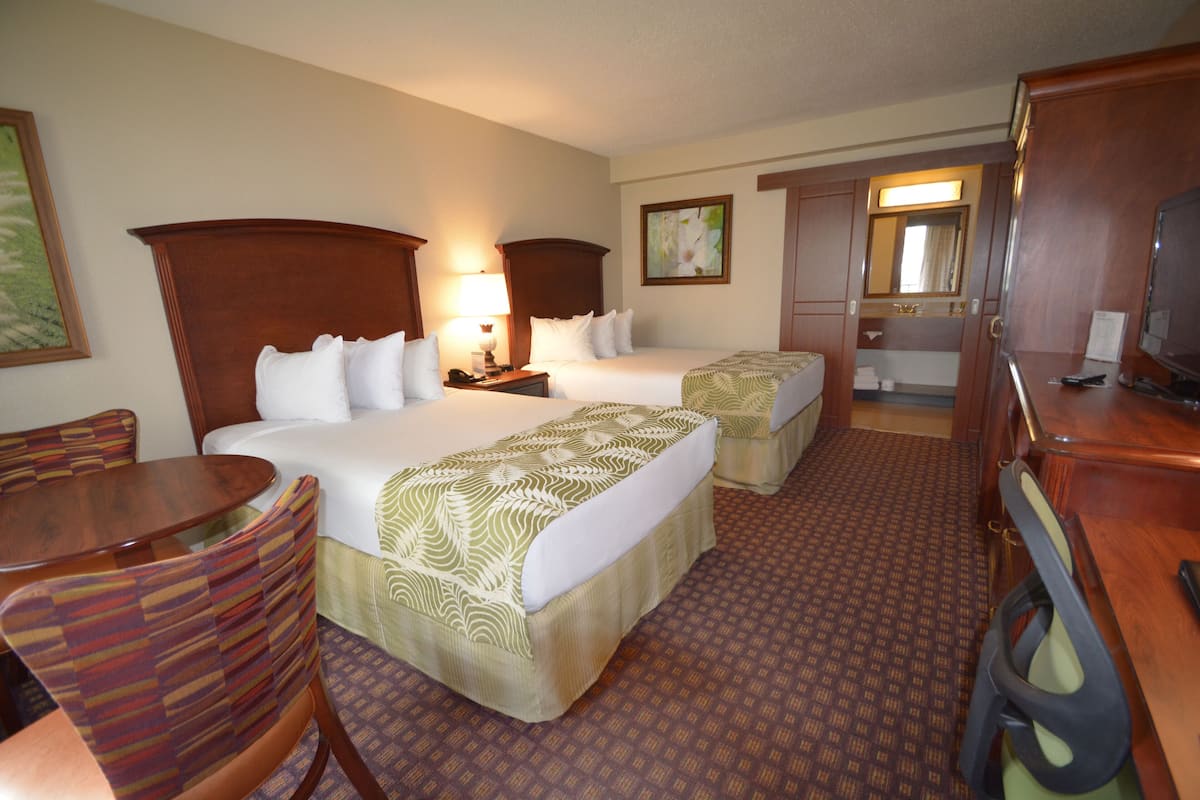 A hotel room with two beds, a desk, a chair, a television, and a bathroom visible through an open door.