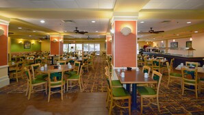 A spacious restaurant with multiple dining tables and chairs, ceiling fans, and a patterned carpet. - Rosen Inn, closest to Universal (Orlando)