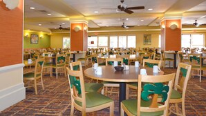 A large dining area with multiple round tables and chairs, ceiling fans, and a patterned carpet.