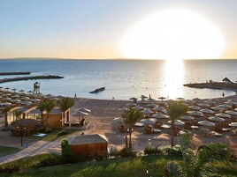 Un complejo turístico en la playa con sombrillas, sillas de descanso y una torre de salvavidas.