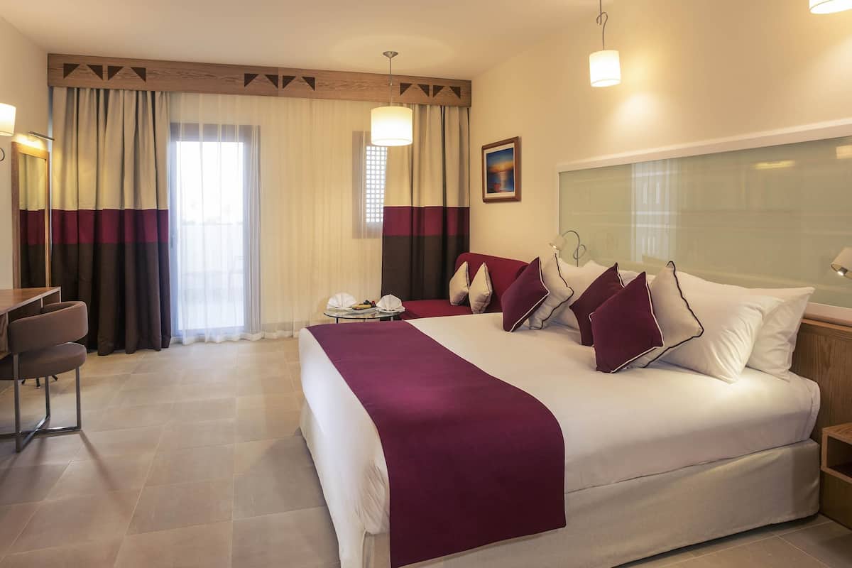 A hotel room with a bed, a desk, a chair, and a window with curtains.