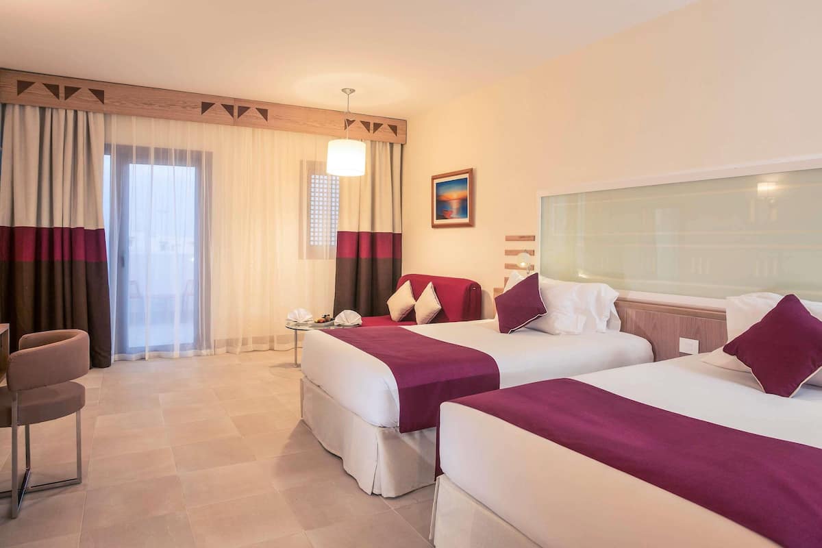 A hotel room with two beds, a desk, a chair, and a window with curtains.