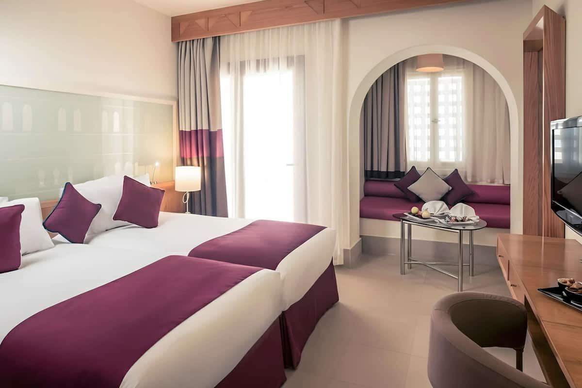 Habitación de hotel con una cama grande, un sofá, un televisor y un escritorio con lámpara.