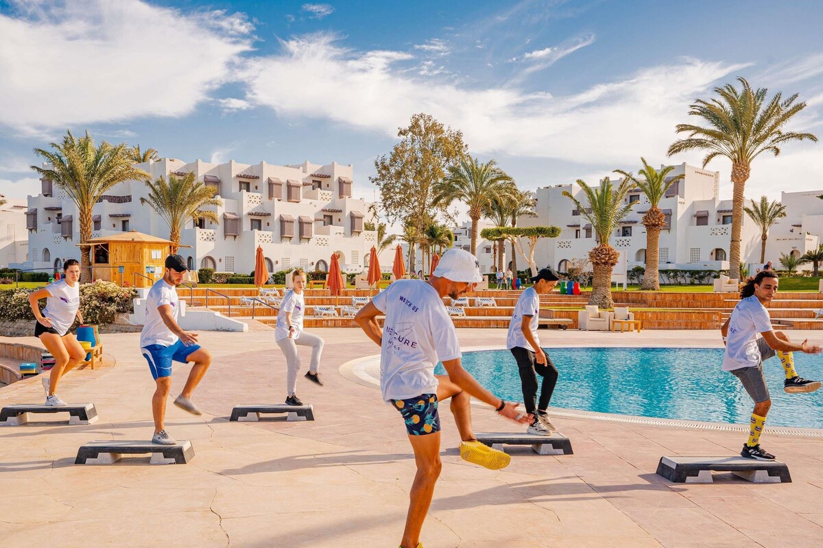 A group of people exercising on stepping platforms by a pool with a resort background.