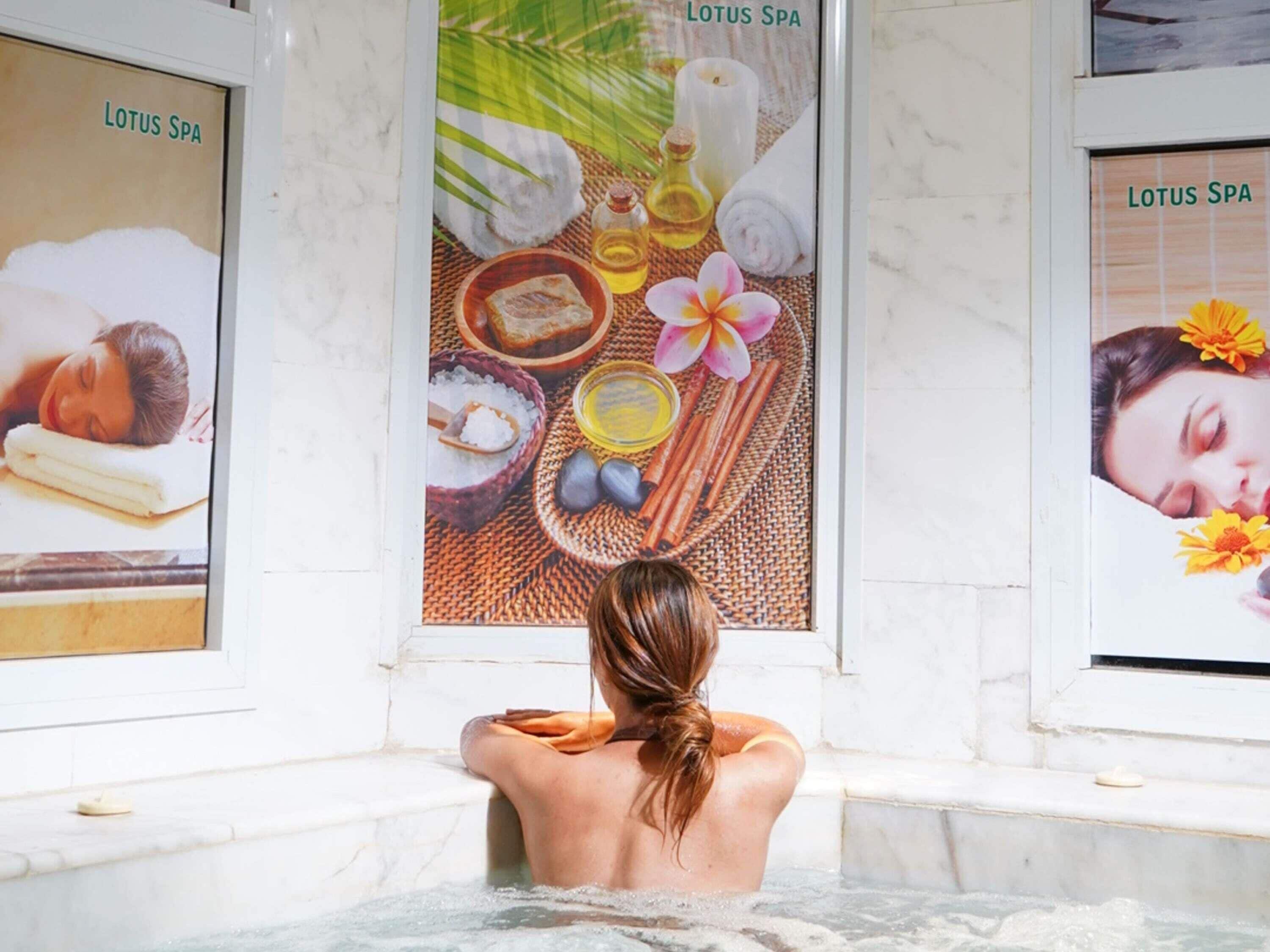 A person relaxing in a spa bath with posters of lotus spa amenities.