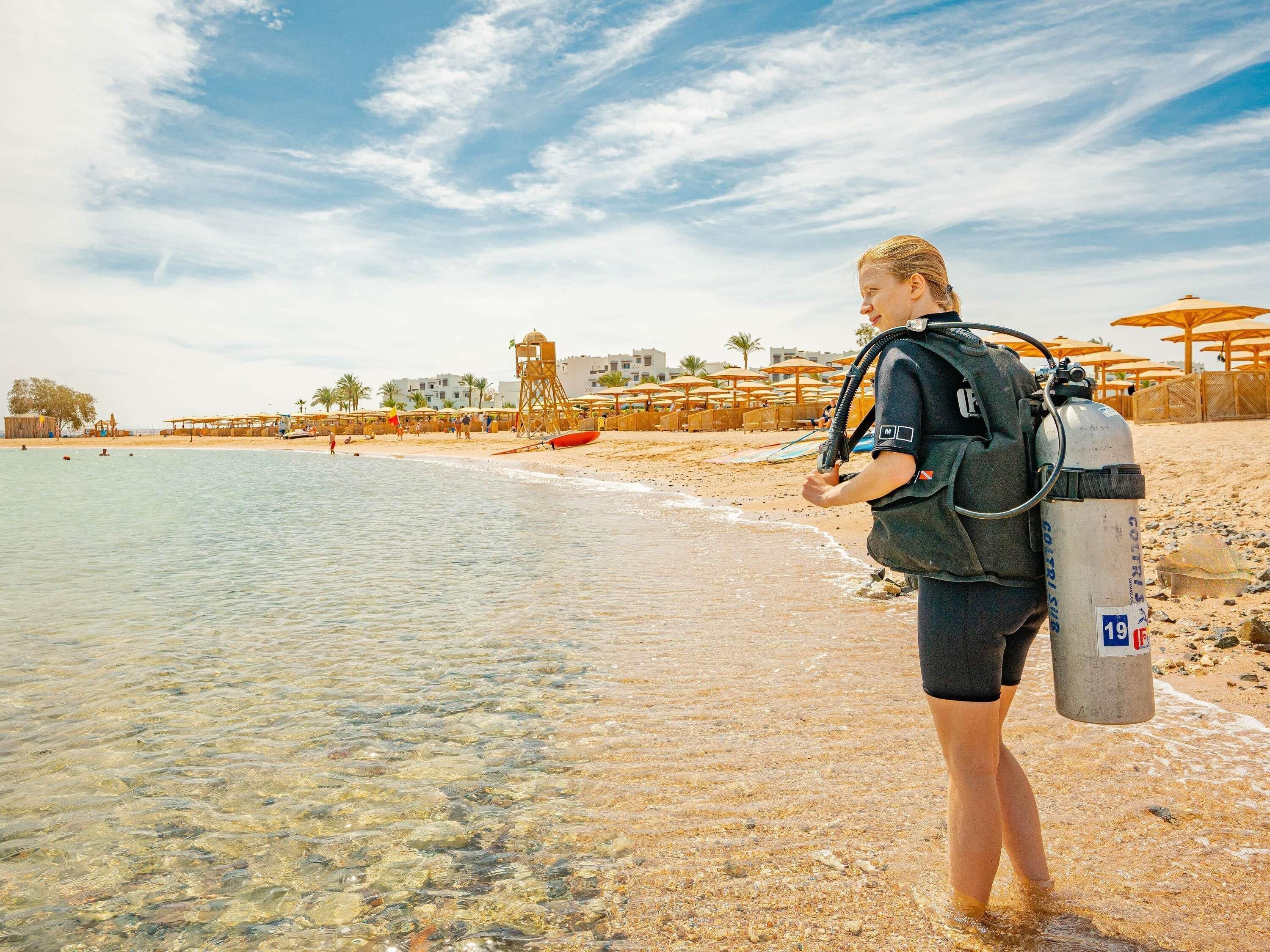 A beach scene with clear shallow waters, a lifeguard tower, umbrellas, and a person in scuba gear.