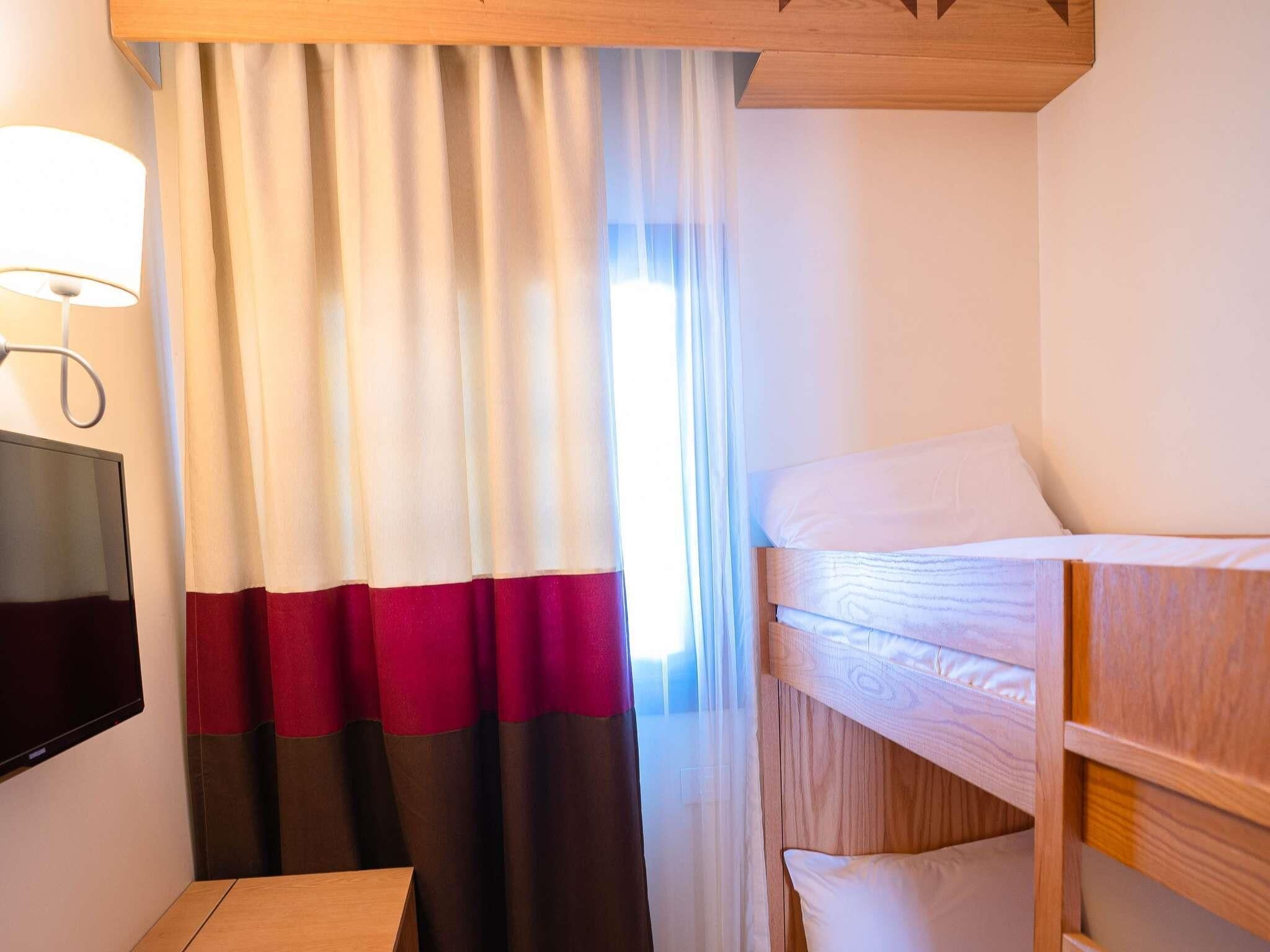 A hotel room with a bed, a TV, and a window with curtains.
