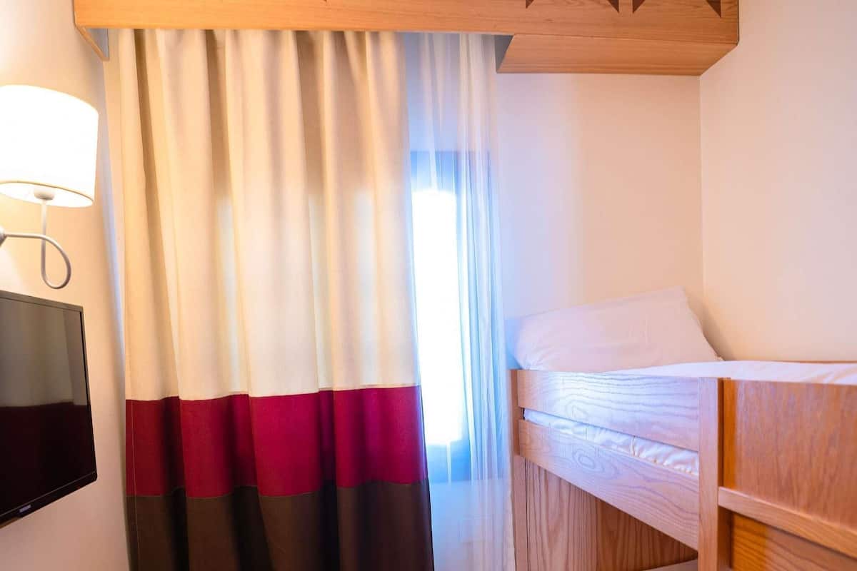 Una habitación de hotel con cama, televisión y ventana con cortinas.
