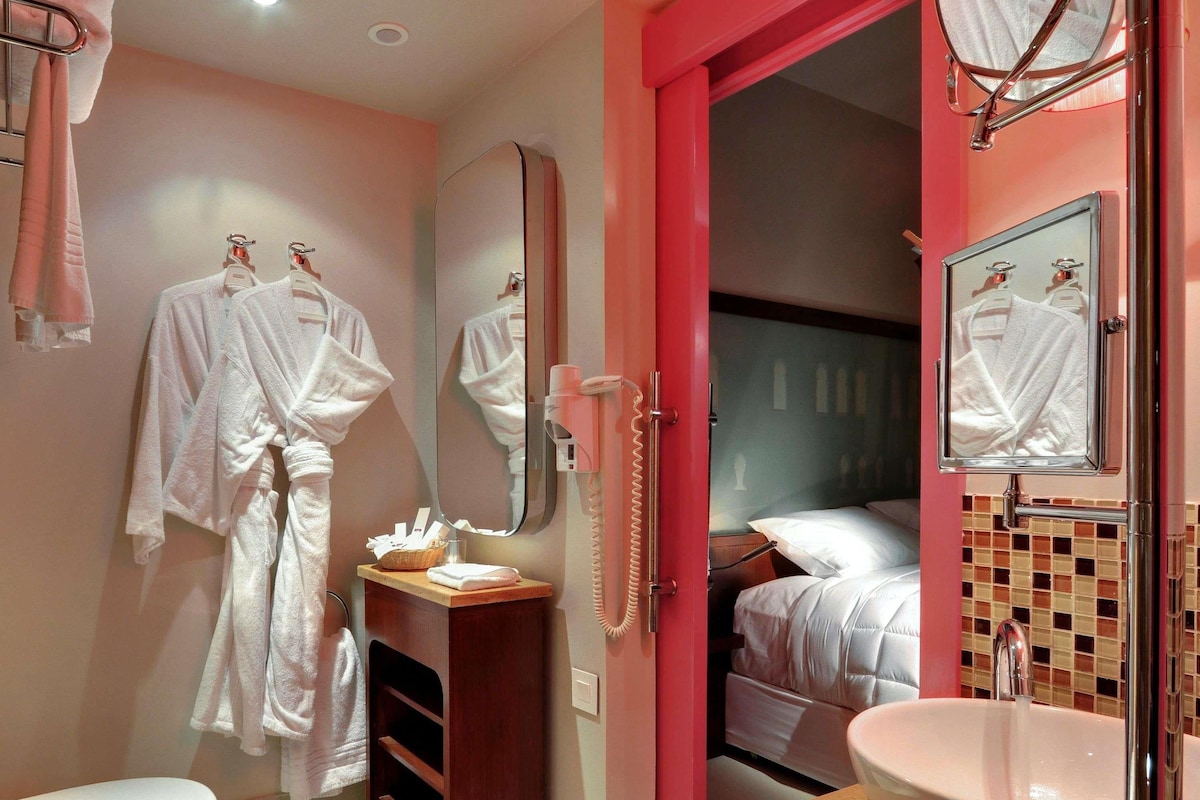 A bathroom with a toilet, sink, and mirror. There are towels and a basket on the counter.