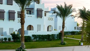 A modern building with white walls and multiple windows, surrounded by well-maintained grass and palm trees. - Mercure Hurghada Hotel (Hurghada)