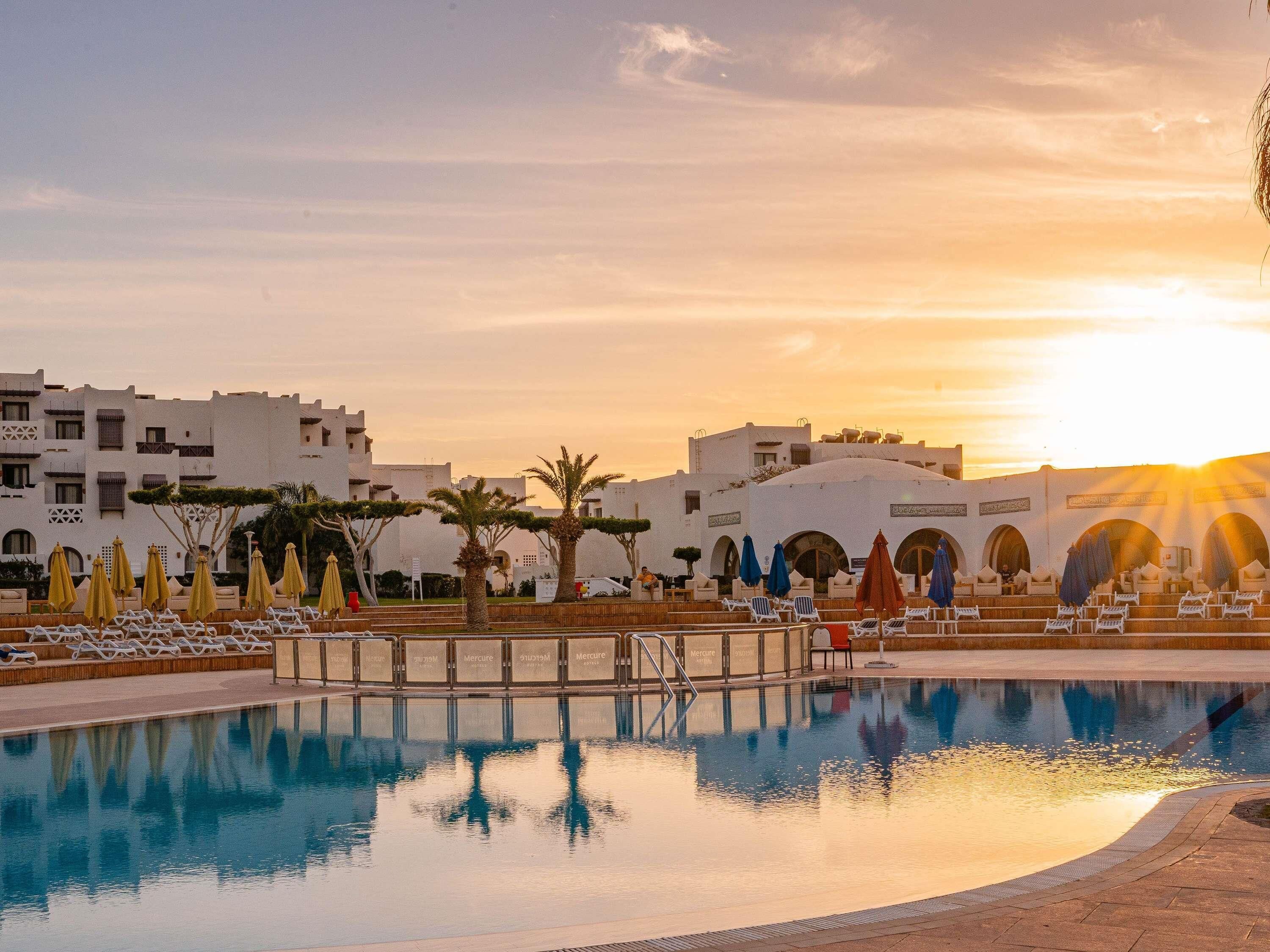A pool area with lounge chairs and umbrellas, surrounded by white buildings with arched windows.