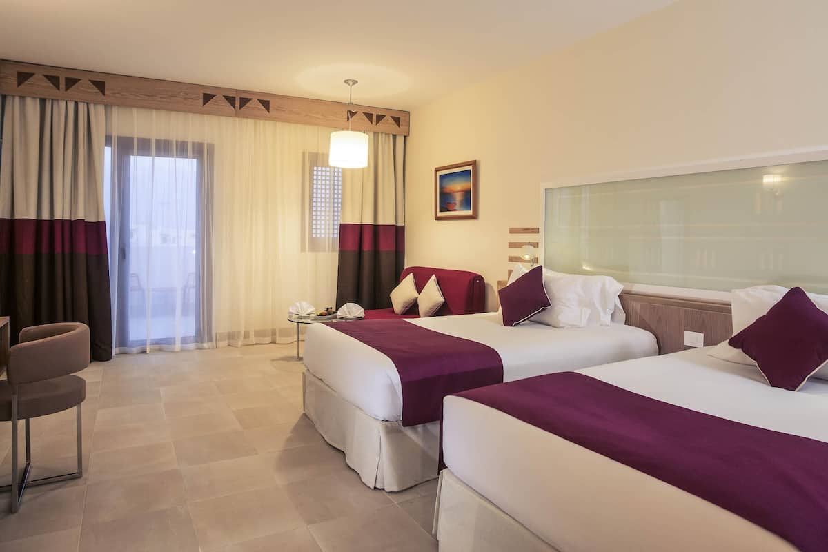 Una habitación de hotel con dos camas, un escritorio, una silla y un ventanal con cortinas.