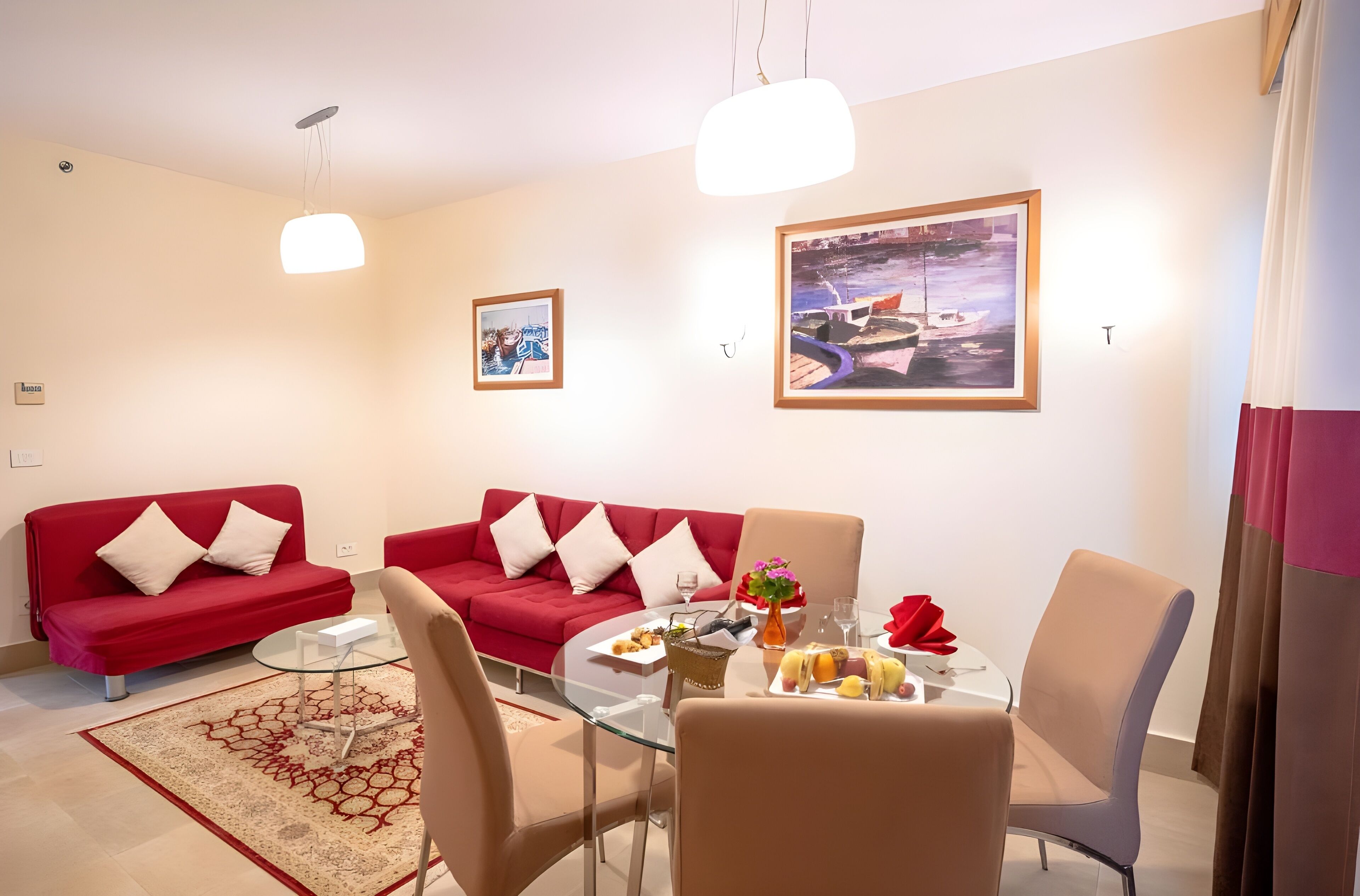 A modern living room with a red sofa, a glass dining table, and a painting on the wall.