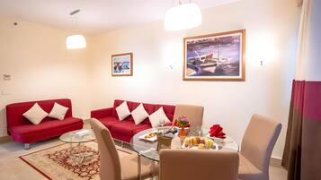 A modern living room with a red sofa, a glass dining table, and a painting on the wall.