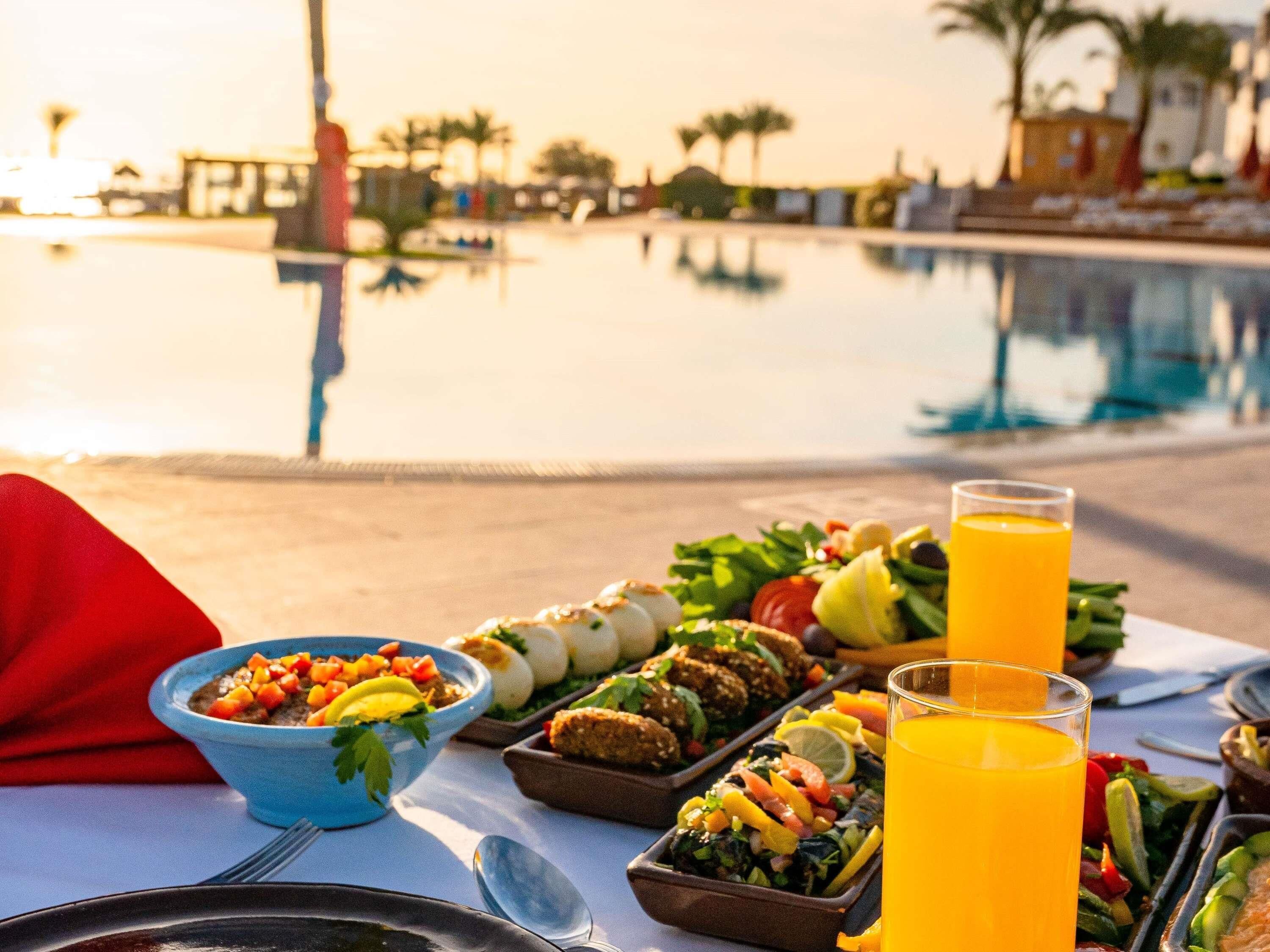 A dining table with various dishes, a glass of orange juice, and a pool in the background.